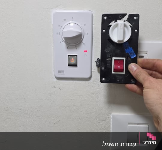 מתגי חשמל על קיר עם יד מחזיקה מתג